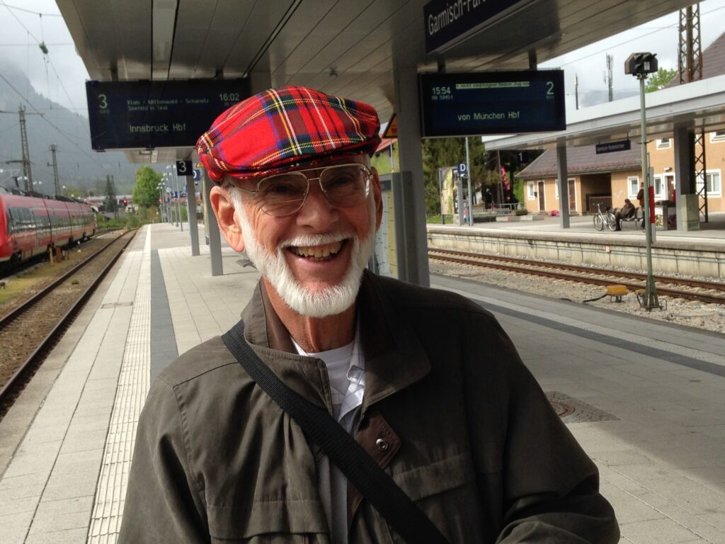 A Person Wearing a Red Plaid Hat and a Green Jacket Standing on a Train Platform