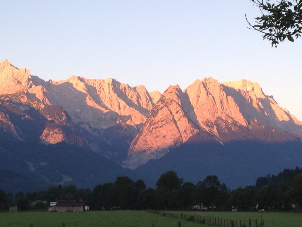 A Photo of a Mountain Range at Sunrise With a Green Field in the Foreground