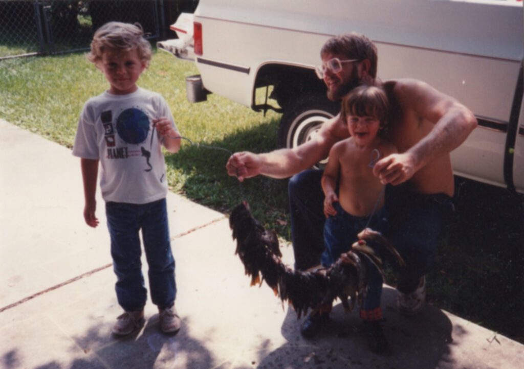 A Man and a Child Holding a Rooster in a Sunny Backyard